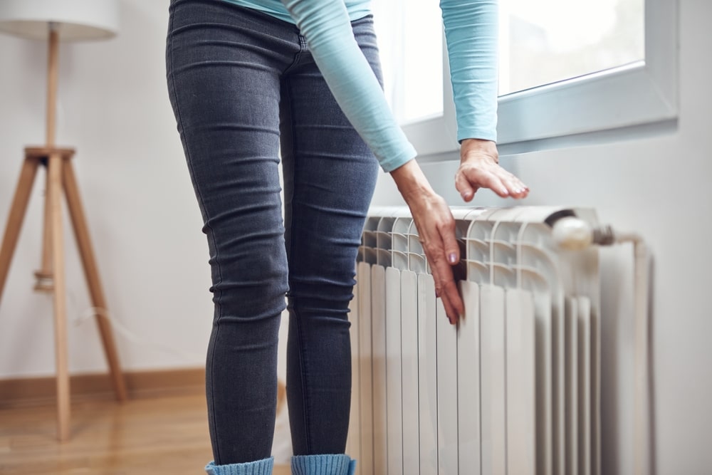 Woman checking boiler efficiency by touching her radiator